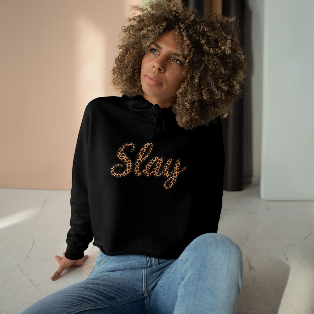 Woman wearing a black hoodie with 'Slay' text, sitting on the floor.