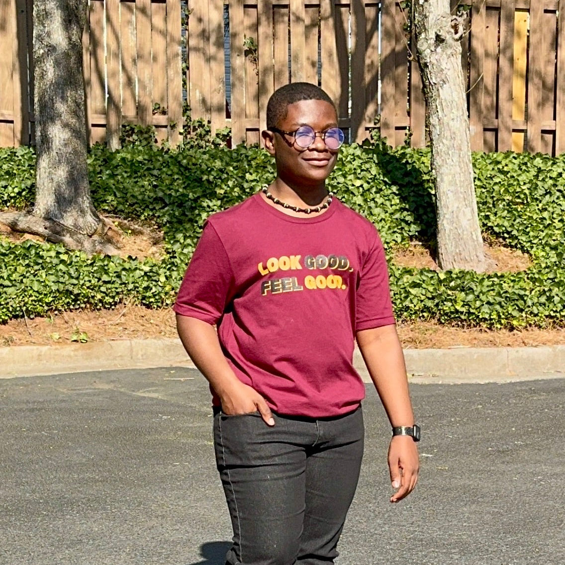 A male smiling wearing a maroon t-shirt with text that says "Look Good. Feel Good." in bold black and gold lettering.
