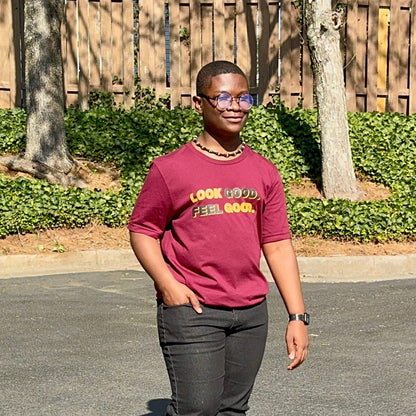 A male smiling wearing a maroon t-shirt with text that says "Look Good. Feel Good." in bold black and gold lettering.