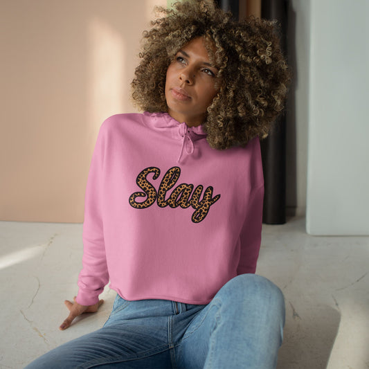 Woman wearing a croppe pink hoodie with leopard print script, 'Slay' text, sitting indoors.