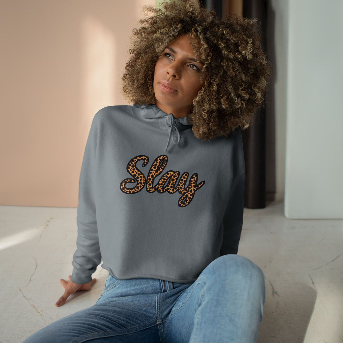 Woman wearing a gray sweatshirt with 'Slay' text, sitting indoors.