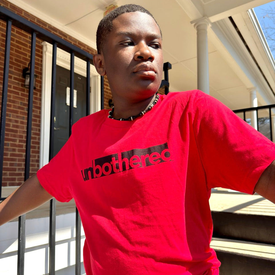 Person wearing a red 'unbothered' graphic t-shirt standing outdoors.
